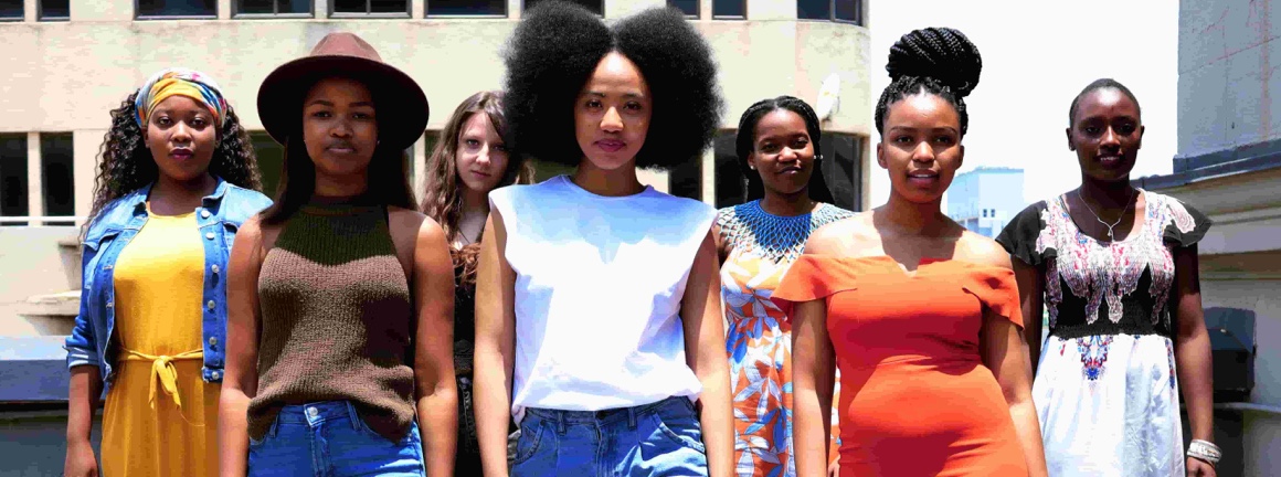 A group of young women posing standing side-by-side on the rooftop of a building.